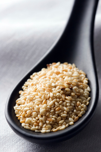 Sesame seeds on a black spoon.