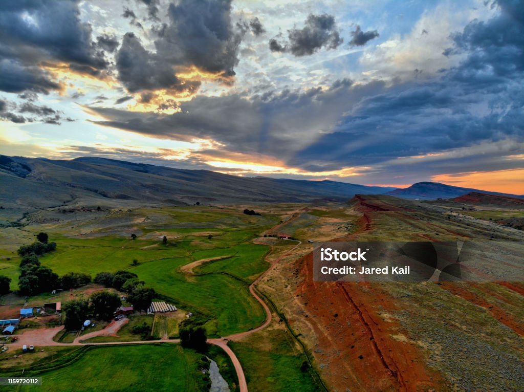 Aerial view of red cliffs, ranch, green fields, and mountains at sunset High drone footage of the Wind River Mountains south of Lander, Wyoming Wyoming Stock Photo