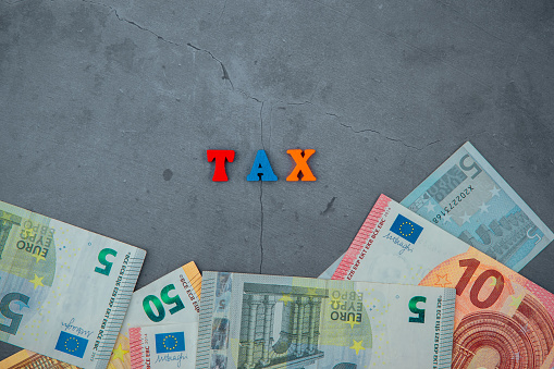 The multicolored tax word is made of wooden letters on a grey plastered wall background