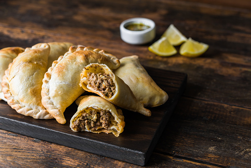 Traditional baked Argentine empanadas savoury pastries with meat beef stuffing against wooden background