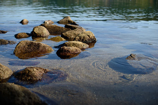 Wet pebbles on seashore in evening sun light. Sea wave on seacoast with round stones.