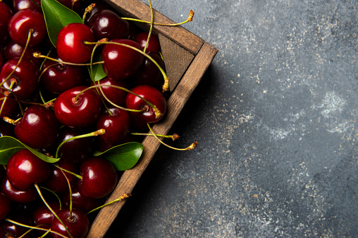 Fresh cherries in a wood container on the paint background.
