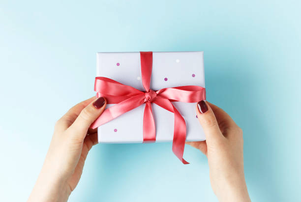 istock Female hands holding gift box with ribbon on blue background, top view 1159739036