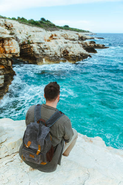istock man with backpack sitting on the cliff enjoying city view 1159739241