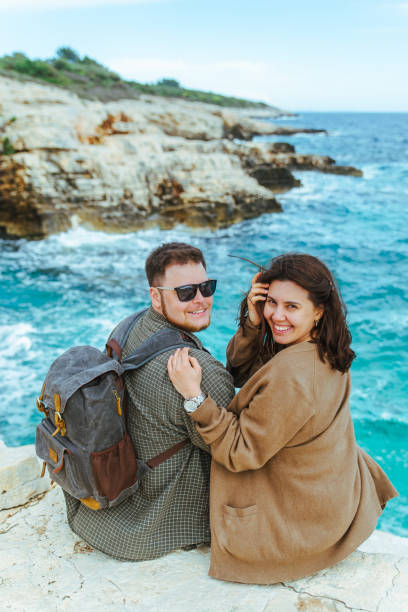 istock couple sitting on the cliff looking at sea 1159739256