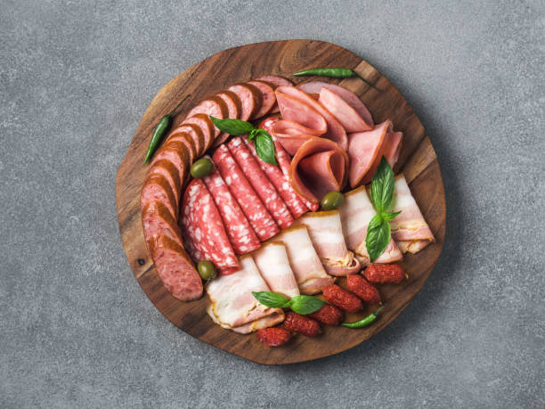 Cold smoked meat platter snacks set Antipasto set platter wooden plate on gray stone. Cold smoked meat plate with sausage, sliced ham,prosciutto,bacon,olives,basil. Appetizer on wooden tray cut tree sawed imitation. Copy space. Top view delicatessen stock pictures, royalty-free photos & images