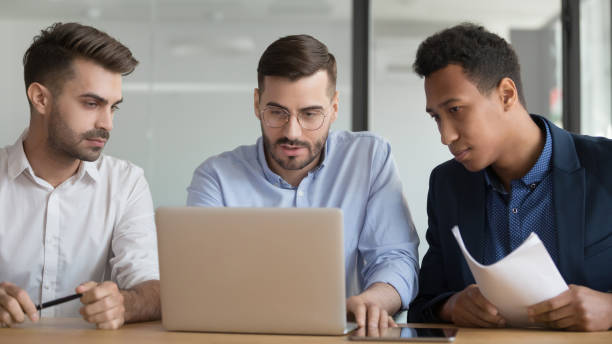 istock Serious male employees work on laptop together at meeting 1159741237