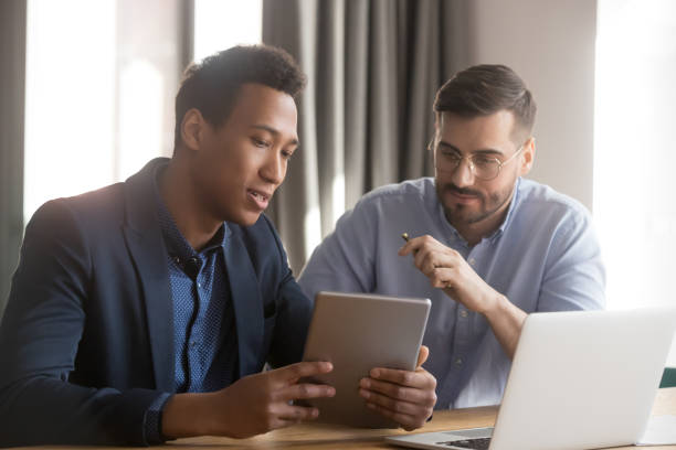 Diverse male colleagues discuss business project using gadgets