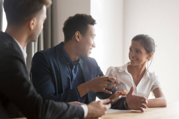 Smiling diverse couple meeting with consultant discussing purchase Smiling diverse couple discussing property buying with real estate agent or broker, ready to sign papers, happy husband and wife meeting with baker or lawyer taking loan or mortgage together independence document agreement contract stock pictures, royalty-free photos & images