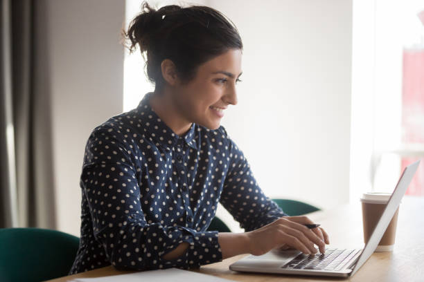 femme indienne de sourire occupée travaillant sur l'ordinateur portatif dans le bureau - typing busy business women photos et images de collection