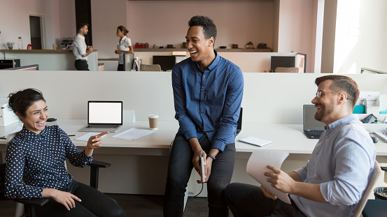 Happy multiethnic employees laugh talking discussing work issues in coworking open space, smiling diverse colleagues have fun joking cooperating in office, chatting at informal team meeting