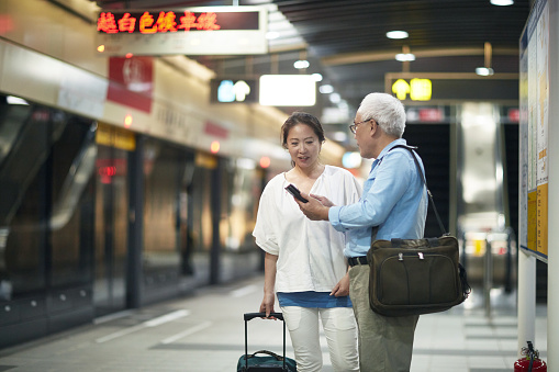Senior Taiwanese couple checking travel options on a smart phone and discussing possible routes to take.