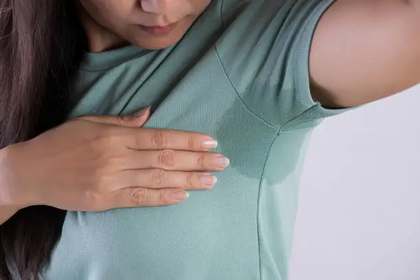 Photo of Close-up asian woman with hyperhidrosis sweating. Young asia woman with sweat stain on her clothes against grey background. Healthcare concept.