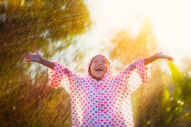 raincoat desgastando da menina asiática feliz da criança que tem o divertimento para jogar com a chuva na luz solar - child autumn nature human face - fotografias e filmes do acervo