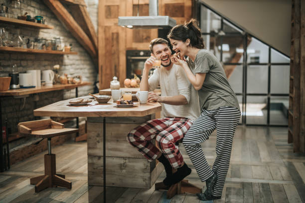 Happy couple having fun during breakfast time at home. Young happy couple spending their morning together in the kitchen while woman is eating and man is drinking juice. tea cup photos stock pictures, royalty-free photos & images