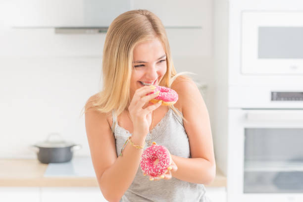 istock Young blonde girl eats pink donuts in home kitchen with taste emotions. 1159751272