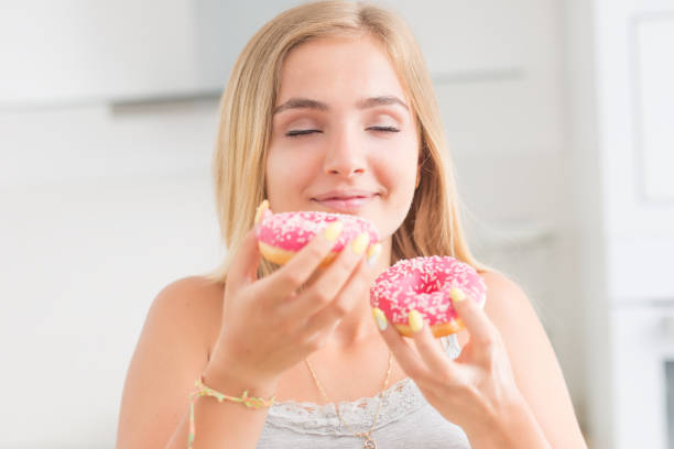 istock Young blonde girl eats pink donuts in home kitchen with taste emotions. 1159751296