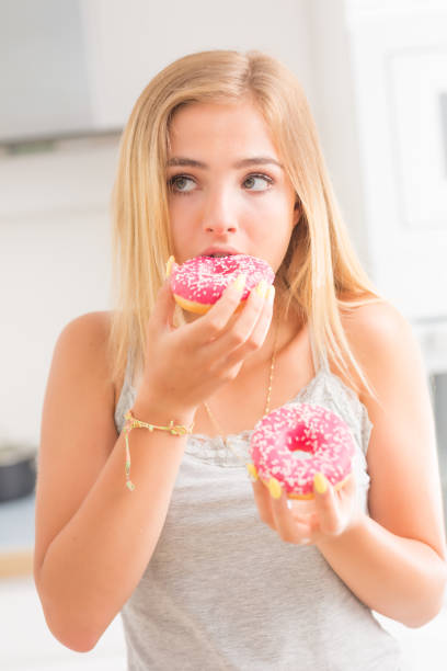 istock Young blonde girl eats pink donuts in home kitchen with taste emotions. 1159751436