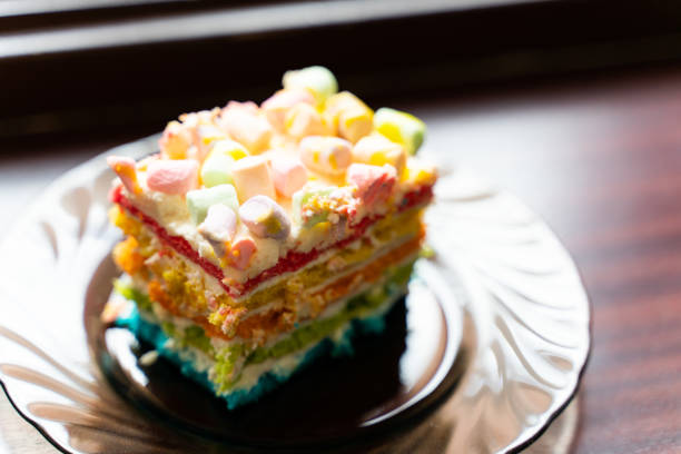 a piece of cake with colored cream sprinkled with marshmallows on a plate close up