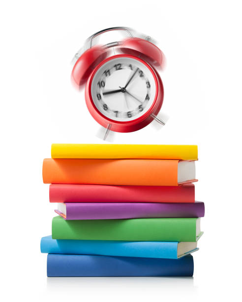 istock Alarm clock ringing on stack of colored books on white background 1159751800