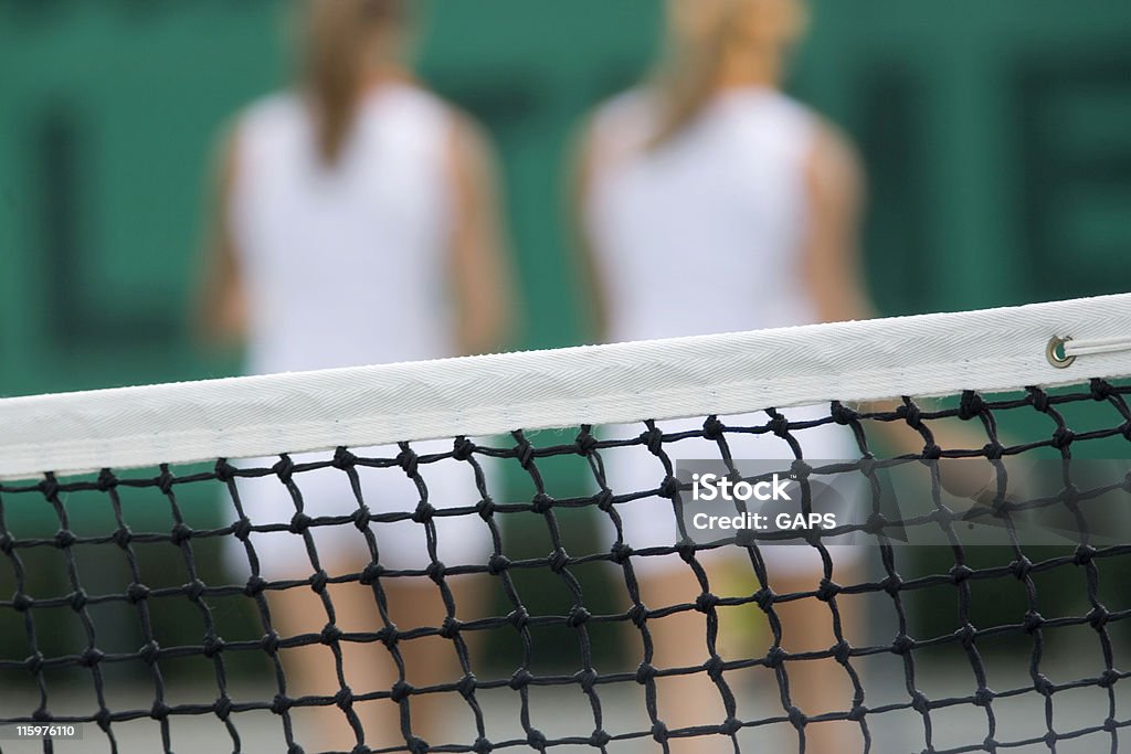 tennis net with the back of two female players tennis net with the back of two female tennis players out of focus in the background Activity Stock Photo