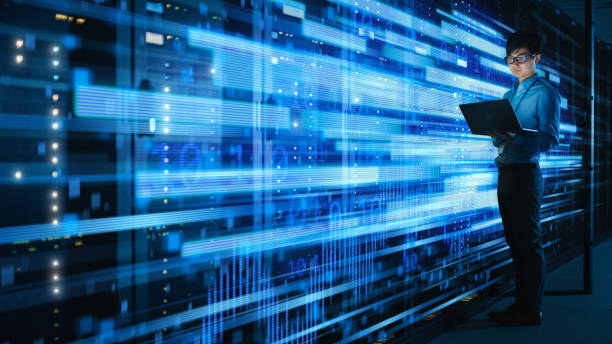 Shot of Asian IT Specialist Using Laptop in Data Center Full of Rack Servers. Concept of High Speed Internet Connections with Blue Visualization Projection of Binary Data Transfer disparo de especialista en ti asiático utilizando el ordenador portátil en el centro de datos lleno de servidores de rack. concepto de conexiones a internet de alta velocidad con proyección de visualización azul de la transferencia de datos binarios