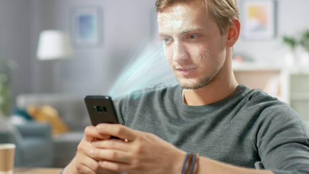 istock Young Man Identified by Biometric Facial Recognition Scanning Process from His Smartphone. Futuristic Concept: Projector Identifies Individual by Illuminating Face by Dots and Scanning with Laser 1159763215