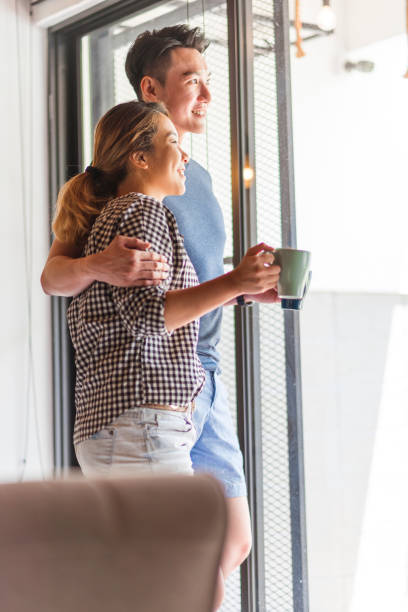 istock Happy young Asian couple standing and looking out through window 1159764934
