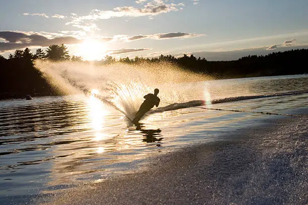 Here's a guy water skiing on a perfect late afternoon. The water is calm with a few small waves. There is a great arch of water spraying into the air giving a dynamic sense of sport and adventure, excitement and fun.