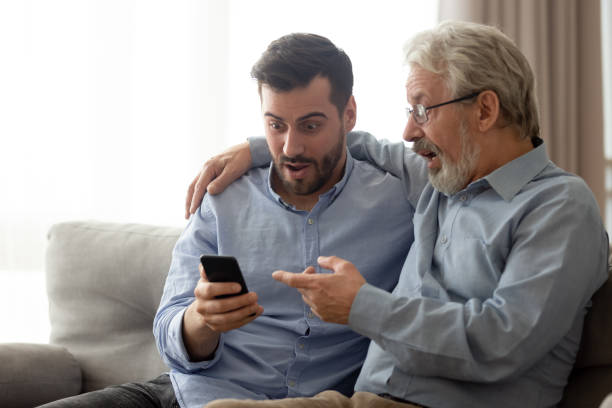 スマートフォンでニュースを読んでショックを受けた先輩の父親を持つ若者 - senior adult relaxation sofa reading �ストックフォトと画像