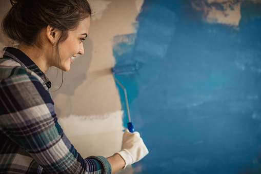 Young happy woman enjoying while painting her walls in blue. Copy space.