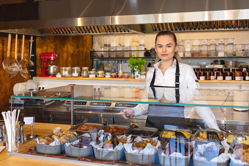 Startup successful small business owner woman working behind counter - Young entrepreneur or waitress serving food - professional catering with worker putting food into buffet.