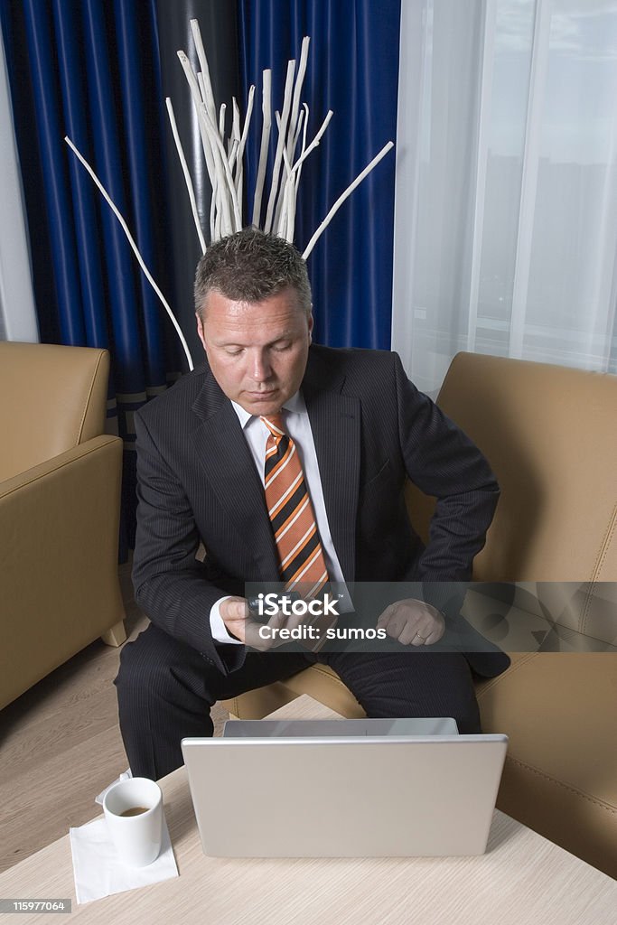 Busy businessman Businessman sitting in sofa texting on his mobile phone with coffee and laptop on table Adult Stock Photo