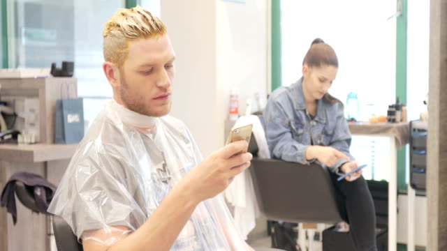 Young Adult Man With Dyed Hair Using Mobile Phone While Waiting in Hair Salon