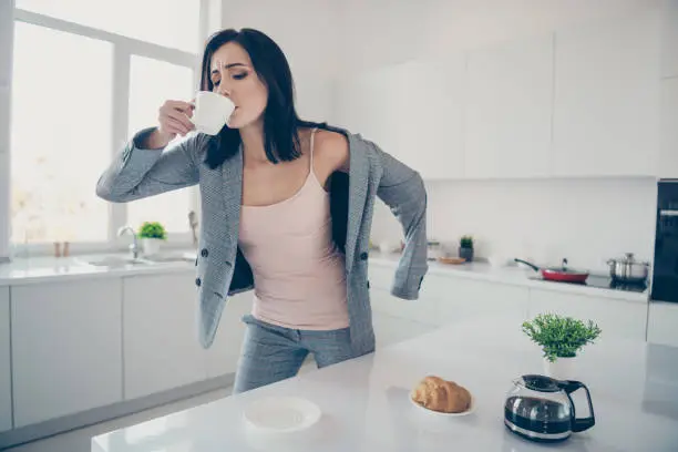 Close up photo beautiful she her lady hot beverage swallow sip croissant, table late job quickly dressing jacket blazer exhausted formal-wear checkered plaid costume bright white kitchen indoors