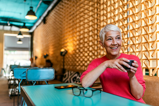Senior businesswoman sitting at a cafe table looking away and thinking. Thoughtful mature female at the coffee shop. Photo of Elegant senior woman thinking in a restaurant. Short hair mature Woman in a coffee shop drinks coffee and thinks about the business.