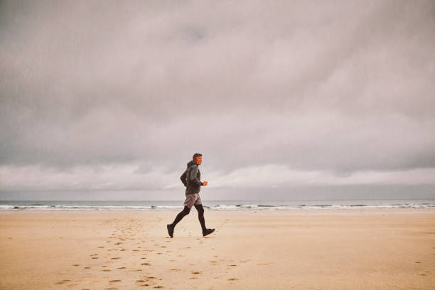 Middle aged man running along a beach on a rainy morning. Added composite rain for extra effect.