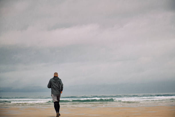 istock Middle aged man running along a beach on a rainy morning. 1159775662