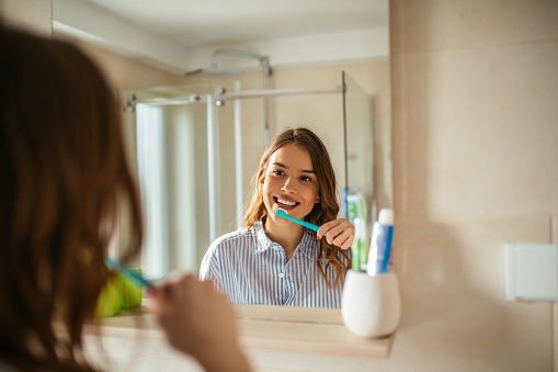 Portrait of beautiful young woman brushing teeth in the bathroom.