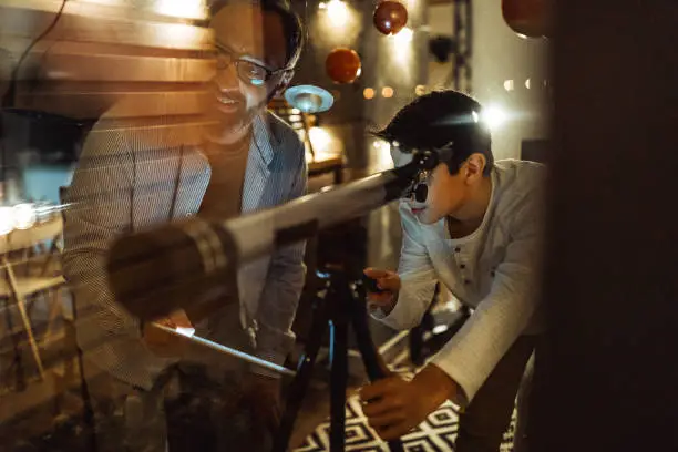 Boy with his father using a telescope  watch the stars through the window