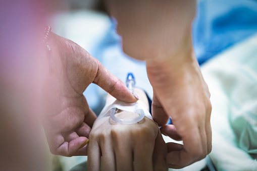 Cropped image of female nurse attaching IV drip on patient hand. Close-up of healthcare worker operating female. They are in hospital ward.