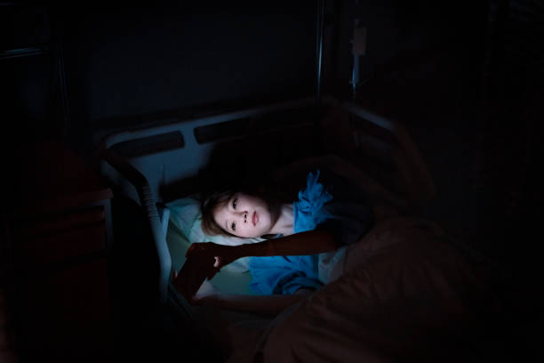Patient using mobile phone while lying on bed High angle view of young female patient using mobile phone on bed. Sick woman resting in darkroom. She is in hospital ward. night hospital bed stock pictures, royalty-free photos & images