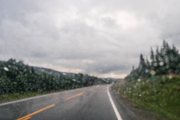 View through the dropped car window to empty road and cloudy natural landscape in Norway. Wet rainy glass, drops on glass, raining concept, motion blur