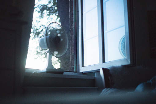 White warm midsummer night in the cozy bedroom in june with ventilator in the open window