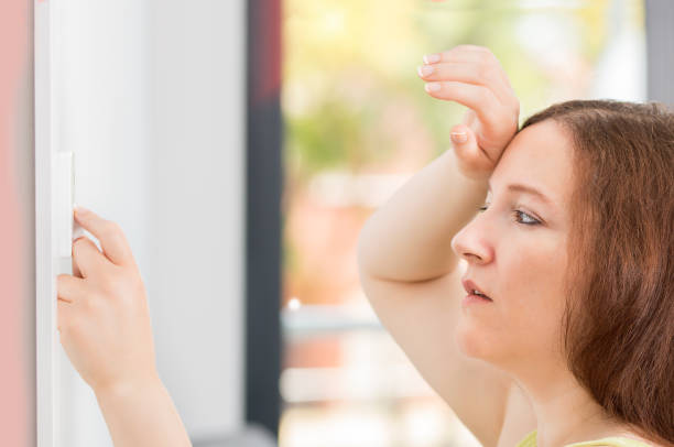 Shot of a side view portrait of a sad woman push button digital thermostat at house and sweating suffering a heat stroke