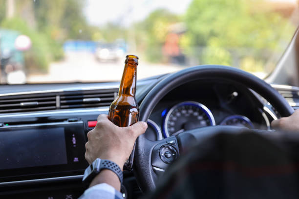 istock man driving car and holding alcohol bottle in another hand while on the road 1159803149