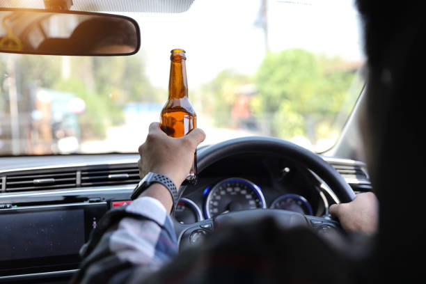 istock man driving car and holding alcohol bottle in another hand while on the road 1159803169