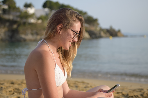 Young happy woman on the beach checking smart phone on line content