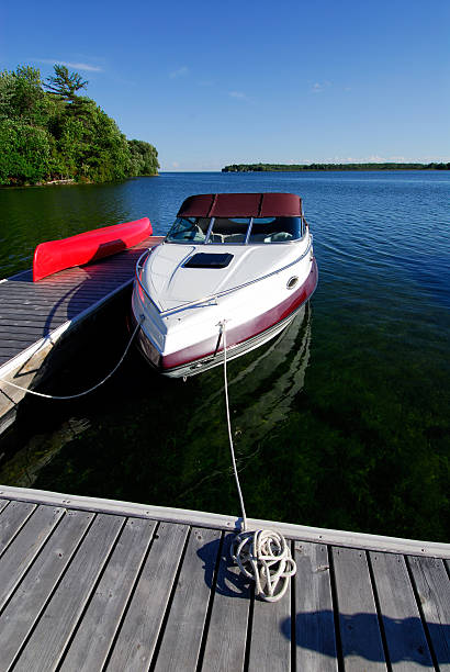 Boat in the water tied to a wooden cottage dock Cabin Cruiser Boat Tied Up At The Cottage Dock On Lake Simcoe, Canada moored stock pictures, royalty-free photos & images