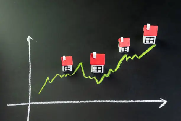 Photo of House, property or real estate market price go up or rising concept, small miniature house with green line graph going up on black chalkboard